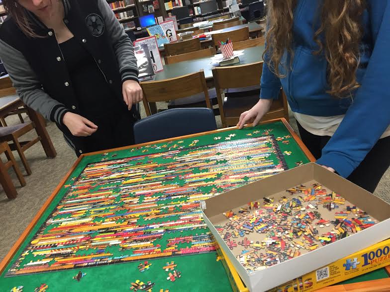Katie Dinkins (17) and Jessica Bautista (19) concentrate on finishing a puzzle in the library during National Library Month.